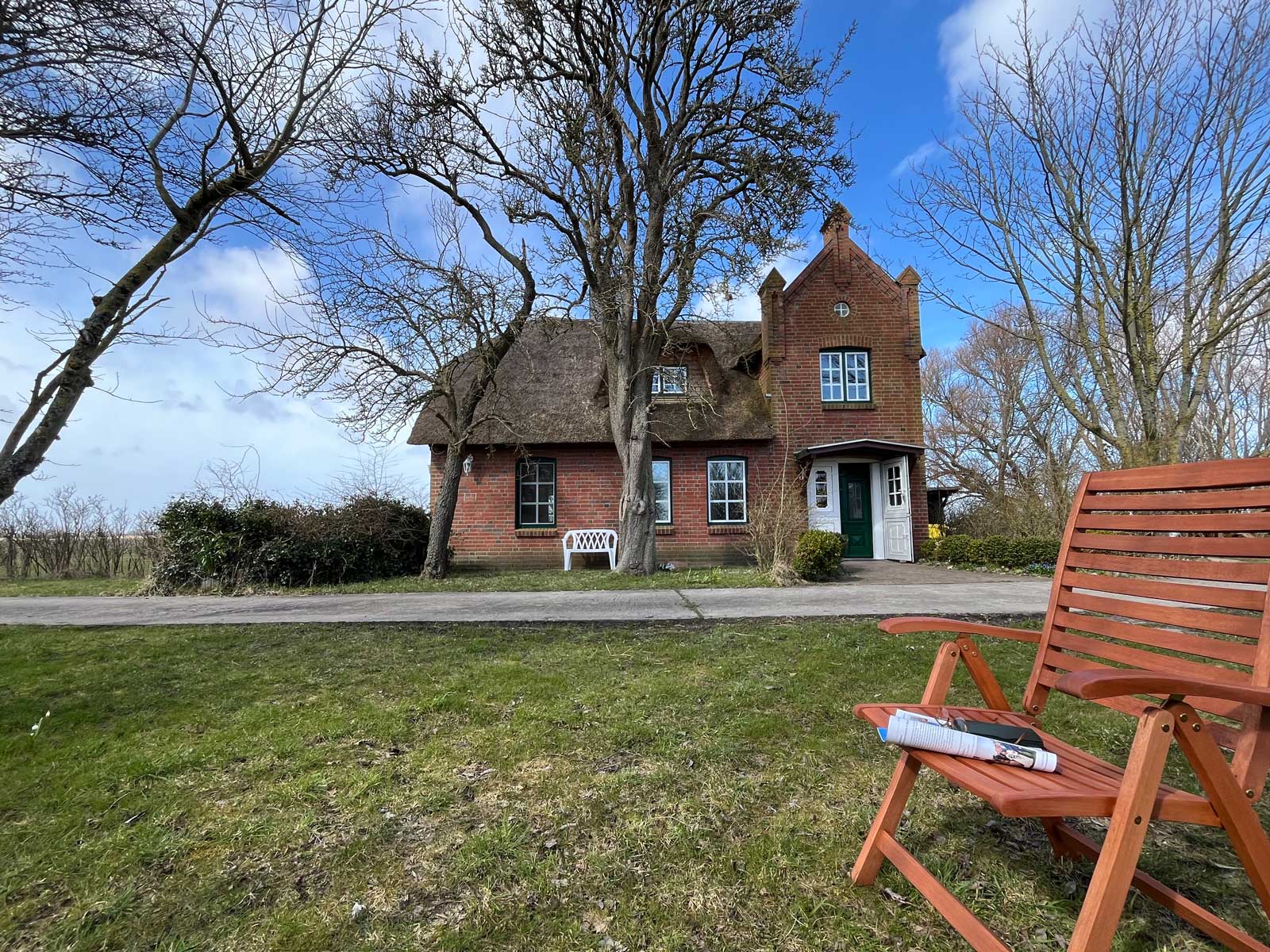 Blick aus dem Garten auf das Deichschlösschen auf Pellworm mit Gartenstuhl und Zeitschrift im Frühling