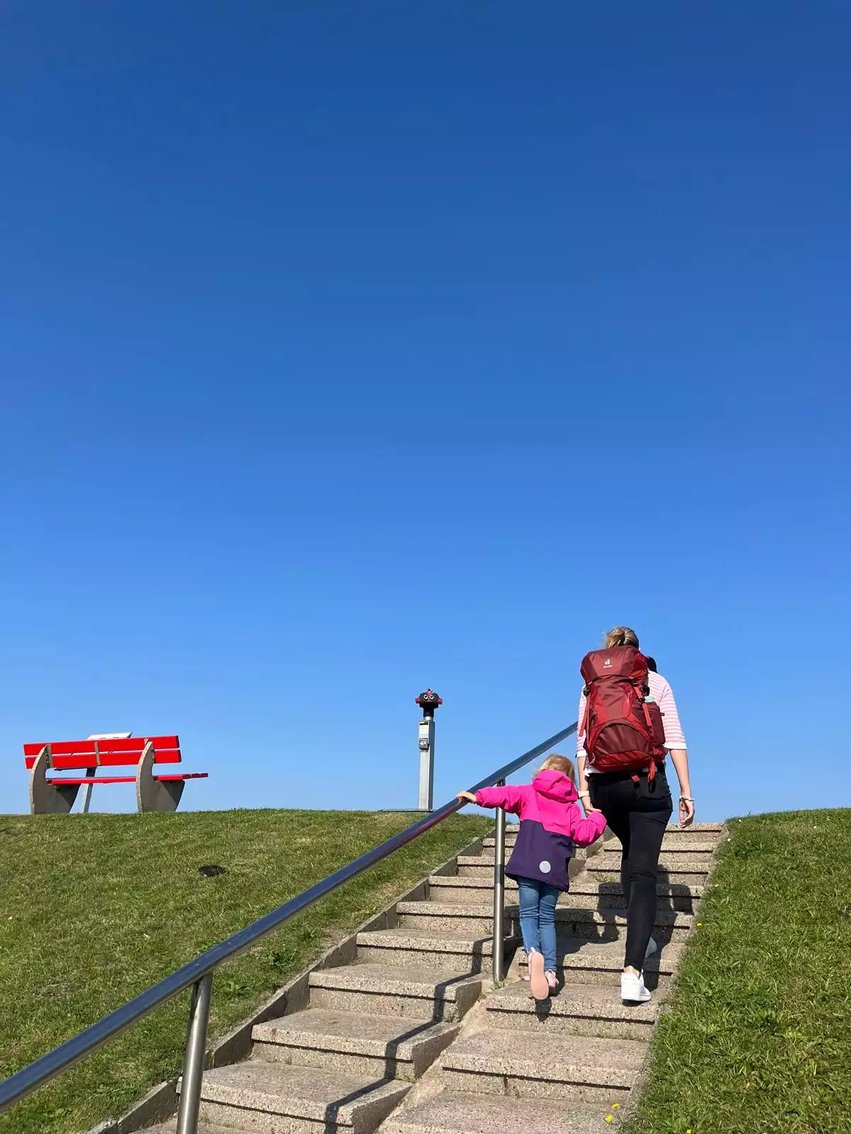 Mutter mit Kind geht den Deichaufgang auf Pellworm hinauf und genießt den Blick auf Watt und Nordsee