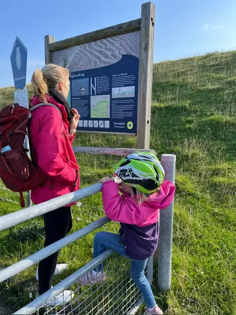 Mutter und Kind lesen gemeinsam eine Infotafel am Deich auf Pellworm und entdecken die Inselnatur