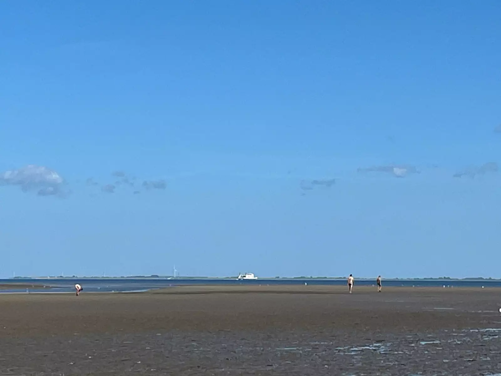 Wattlandschaft auf Pellworm mit blauer Himmel, Fähre und Wattwanderern in der Ferne