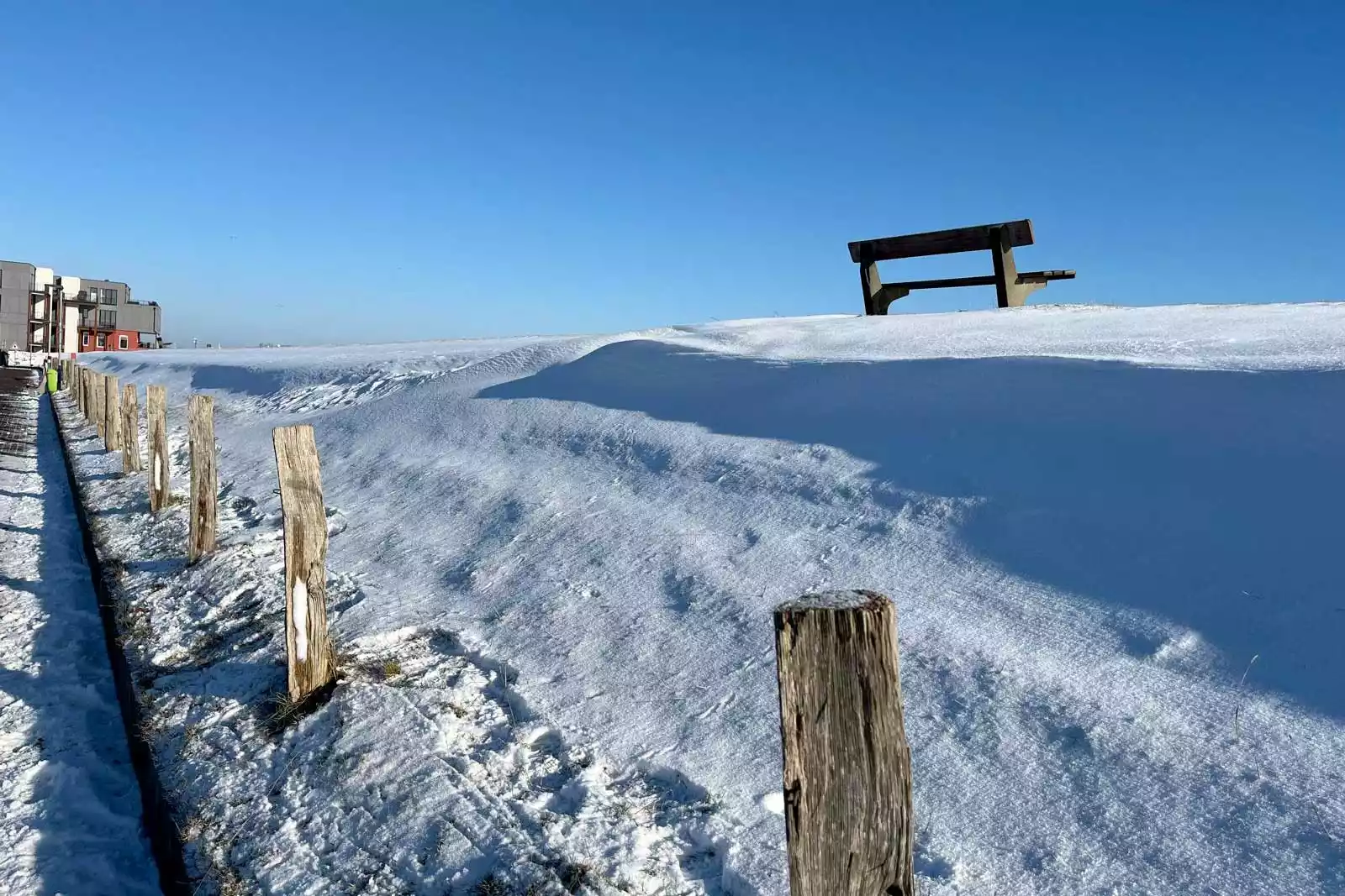 Verschneiter Deich und einer Bank für Pausen während langer Spaziergänge im Winterurlaub