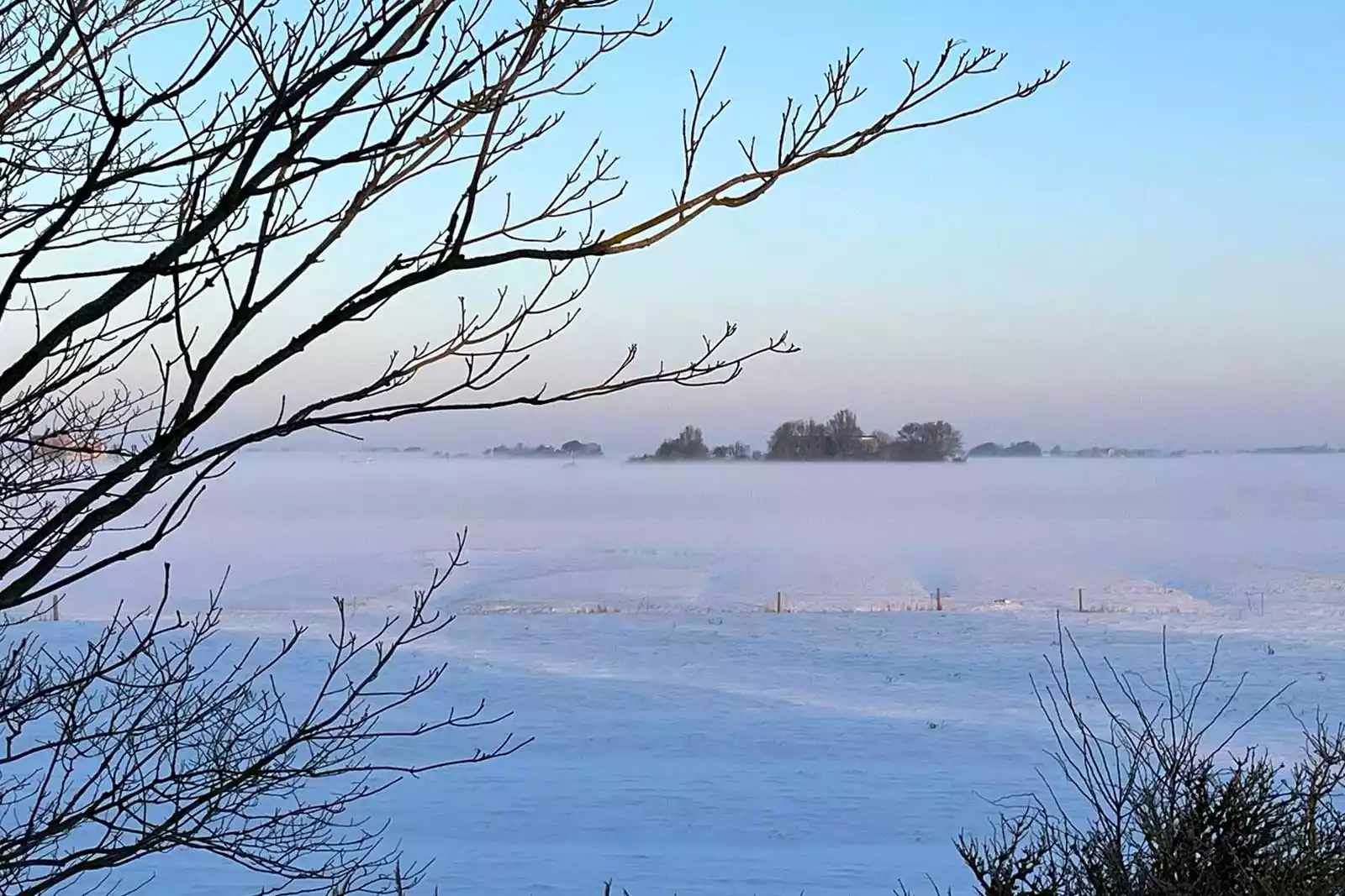 Winterlandschaft auf Pellworm mit rötlichem Sonnenuntergang am Horizont über weiter Nordseeinsel