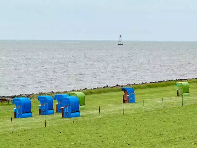 Grüner Deich mit Strandkörben am Strand vom Pellwormer Leuchtturm