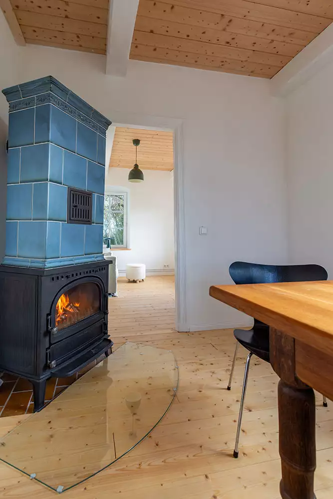 Esszimmer im Ferienhaus Deichschlösschen mit brennendem Kachelofen und Blick ins Lesezimmer